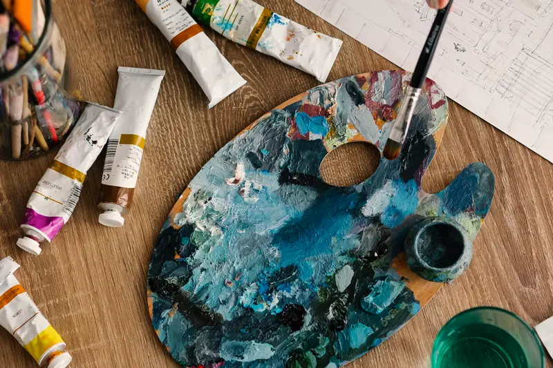 An artist's palette with paint tubes and brushes on a wooden table