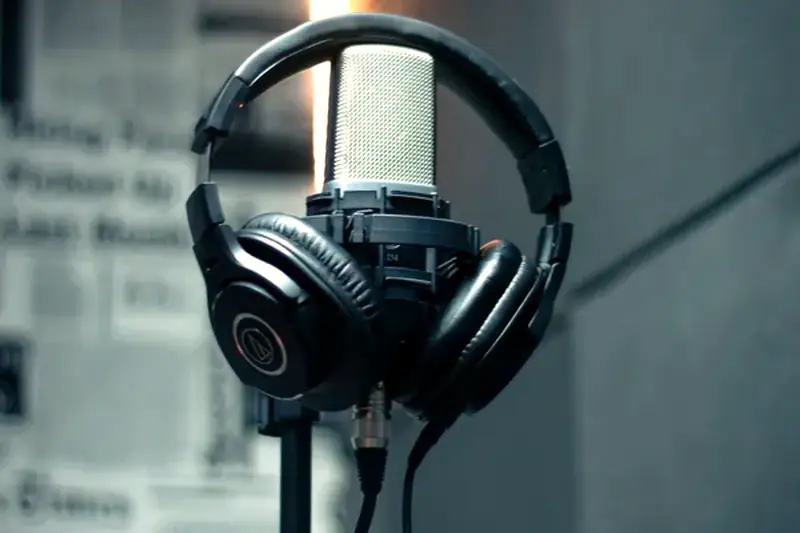 A studio microphone with headphones hanging beside it