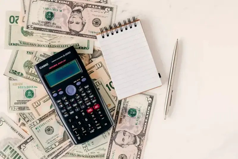 A calculator, notebook, and US dollar bills laid out for budgeting