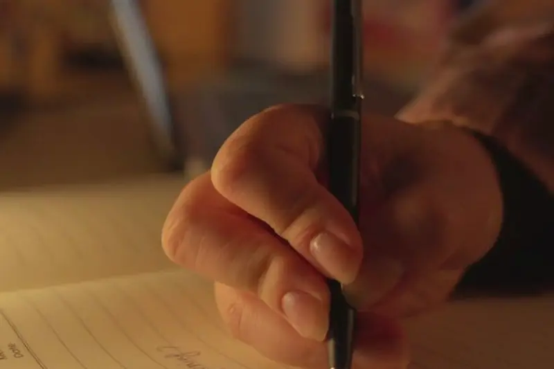 A hand writing a video script with a pen in a notebook, close up