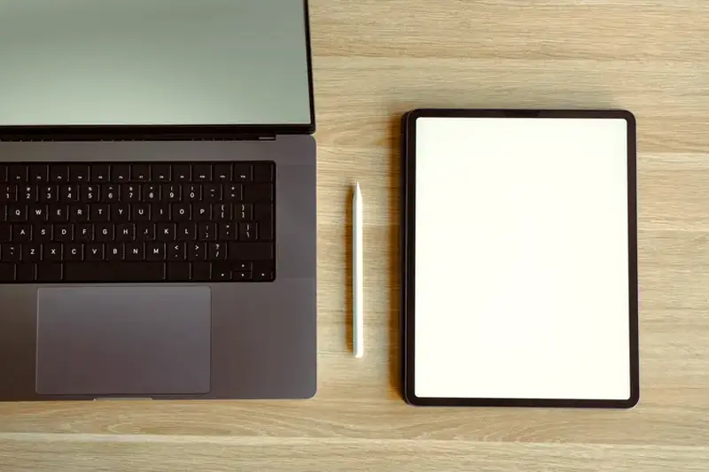 A laptop and a tablet with a blank white screen on a wooden desk