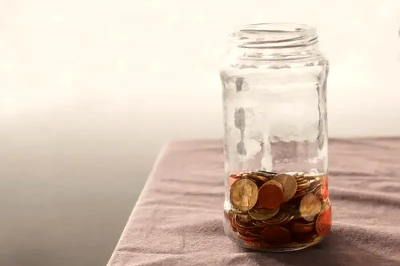 A glass jar with coins saved inside it on a table