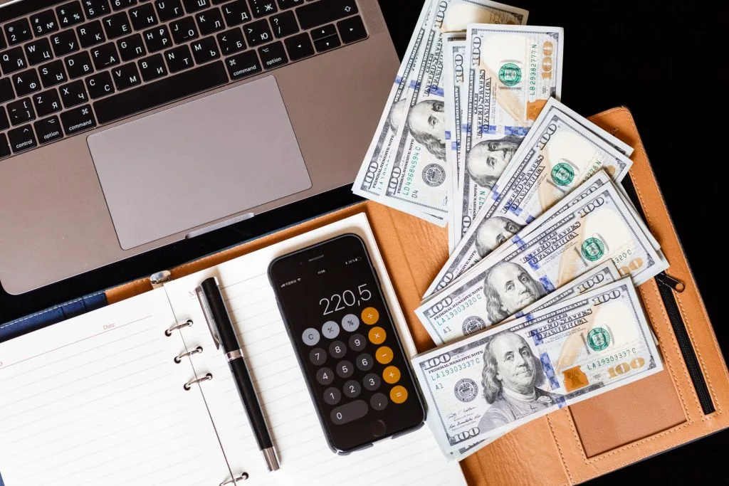 A desk with a laptop, calculator, cash and a phone, working out what a channel earns