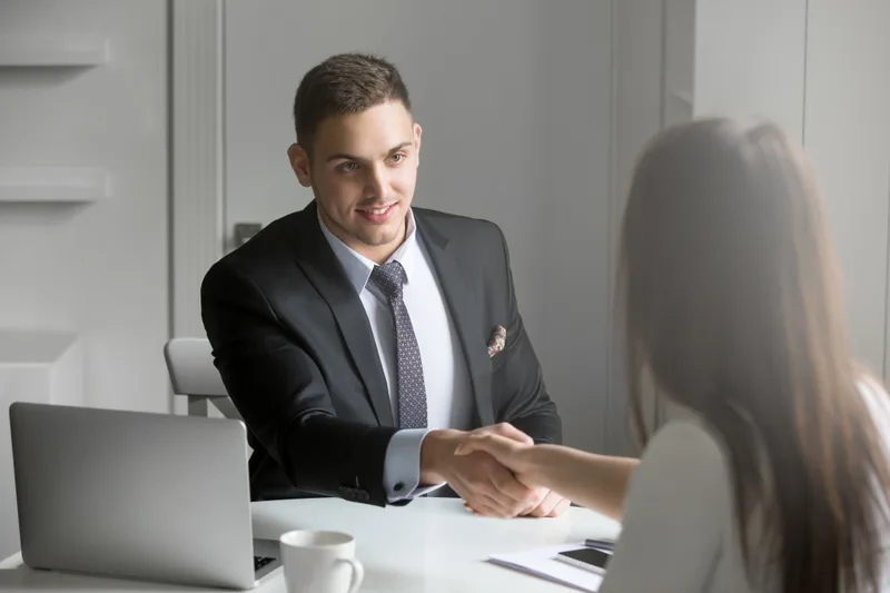 A job candidate shaking hands with an interviewer across a desk at a job interview
