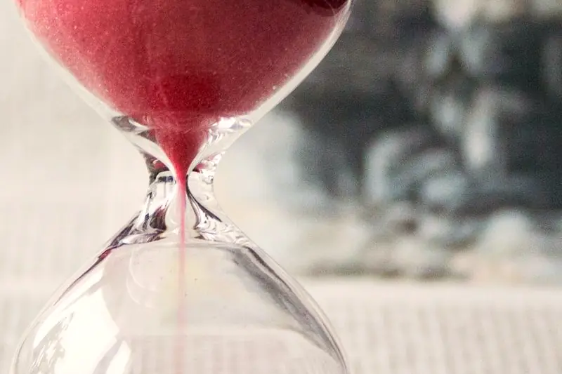 An hourglass with pink sand running through it, close up
