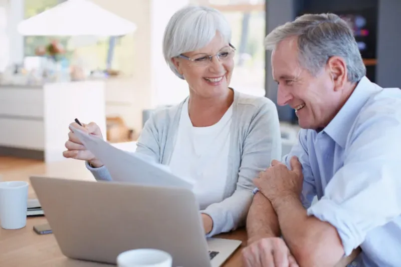 A retired couple reviewing paperwork together beside a laptop at home