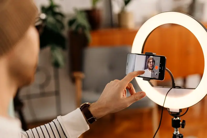 A creator adjusting a smartphone mounted in a ring light to record a short video
